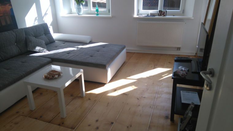 Ein Wohnzimmer mit einem grauen Ecksofa, einem weißen quadratischen Couchtisch und einem Holzboden
