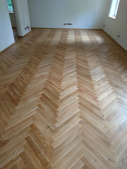 Ein Zimmer mit hellen, naturfarbenen Holzböden im klassischen Fischgrätmuster, aus der Vogelperspektive betrachtet.