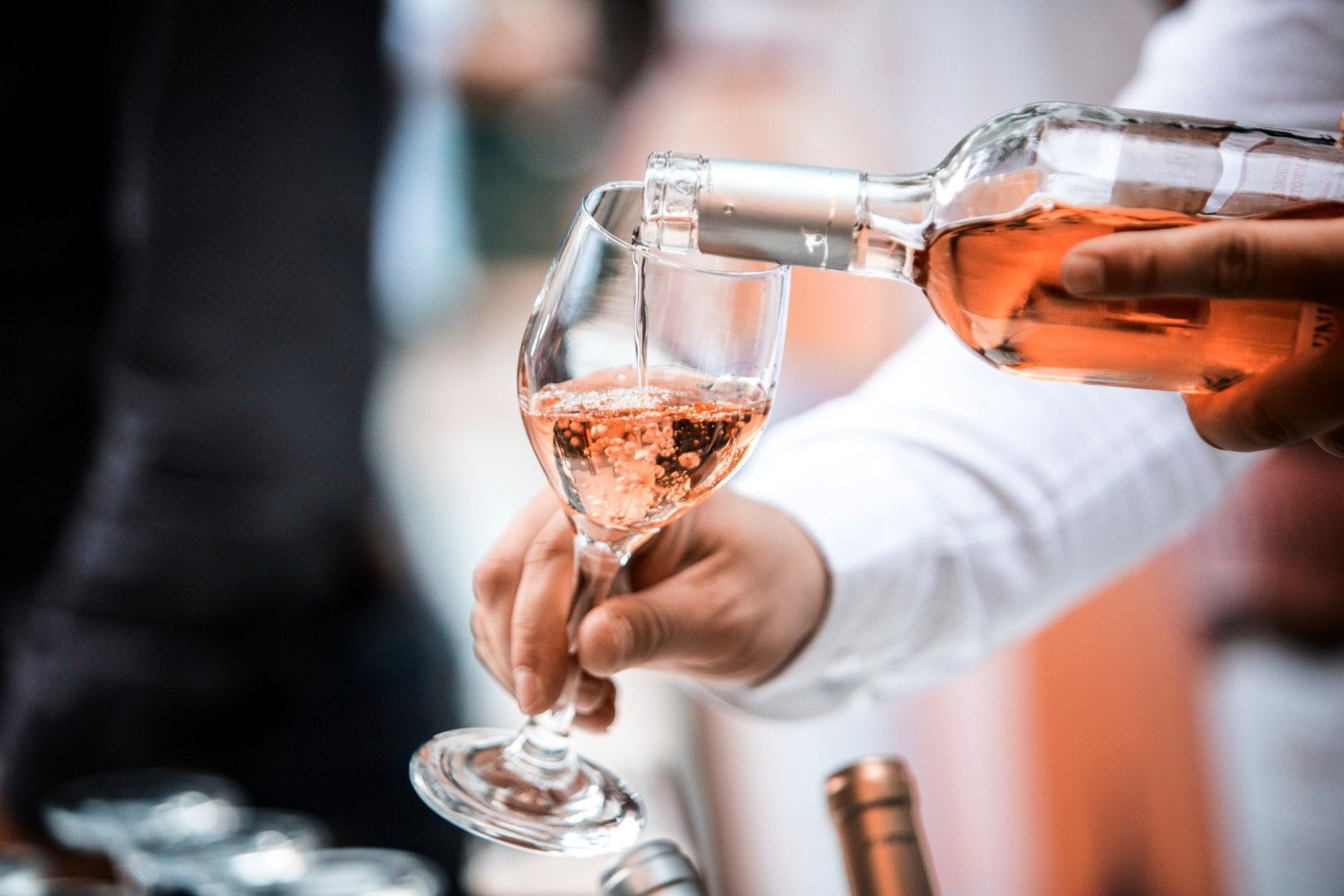 Une main verse du vin rosé dans une flûte à champagne lors d’une réception officielle
