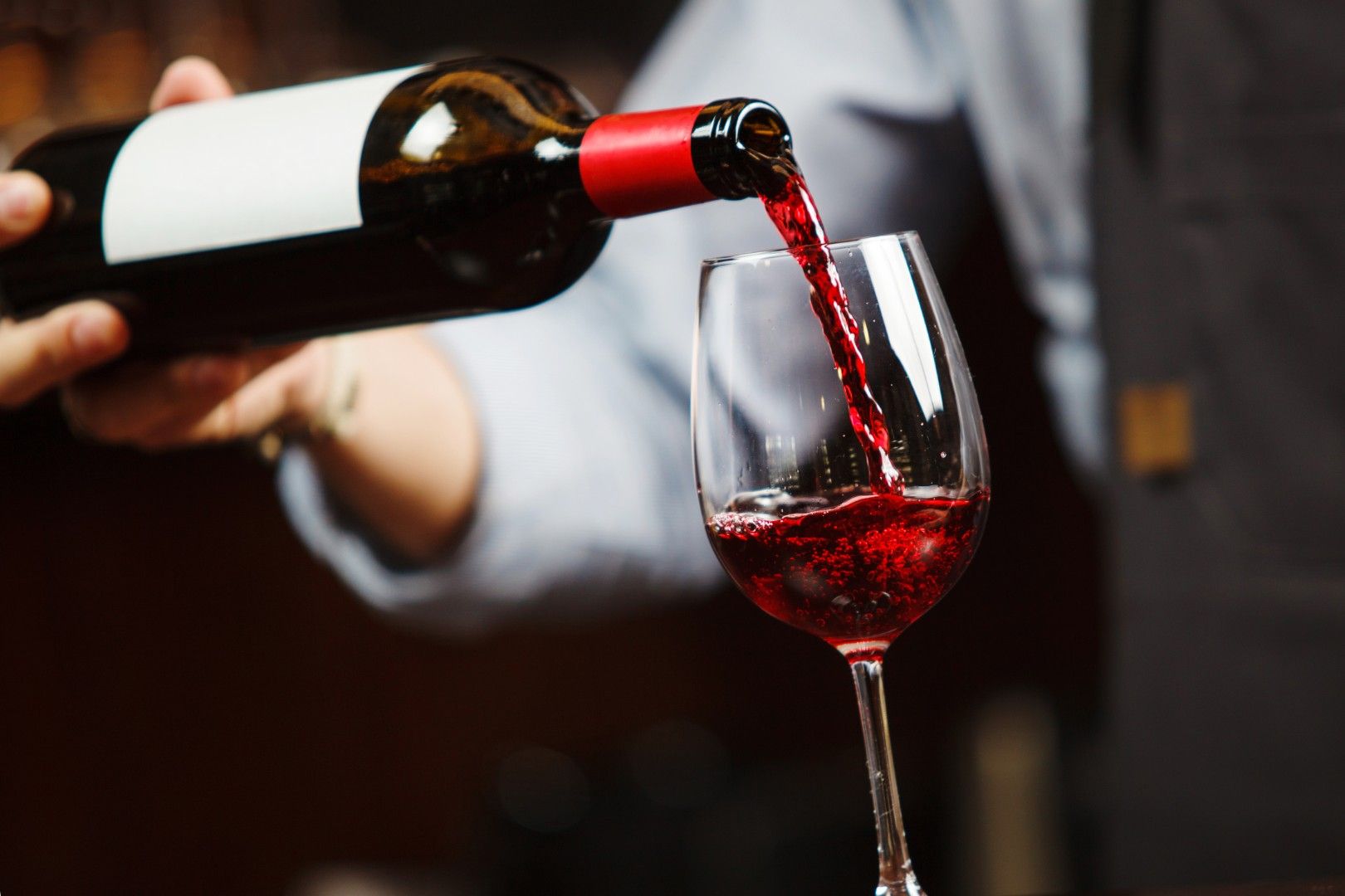 Du vin versé d’une bouteille dans un verre, avec une personne floue en arrière-plan