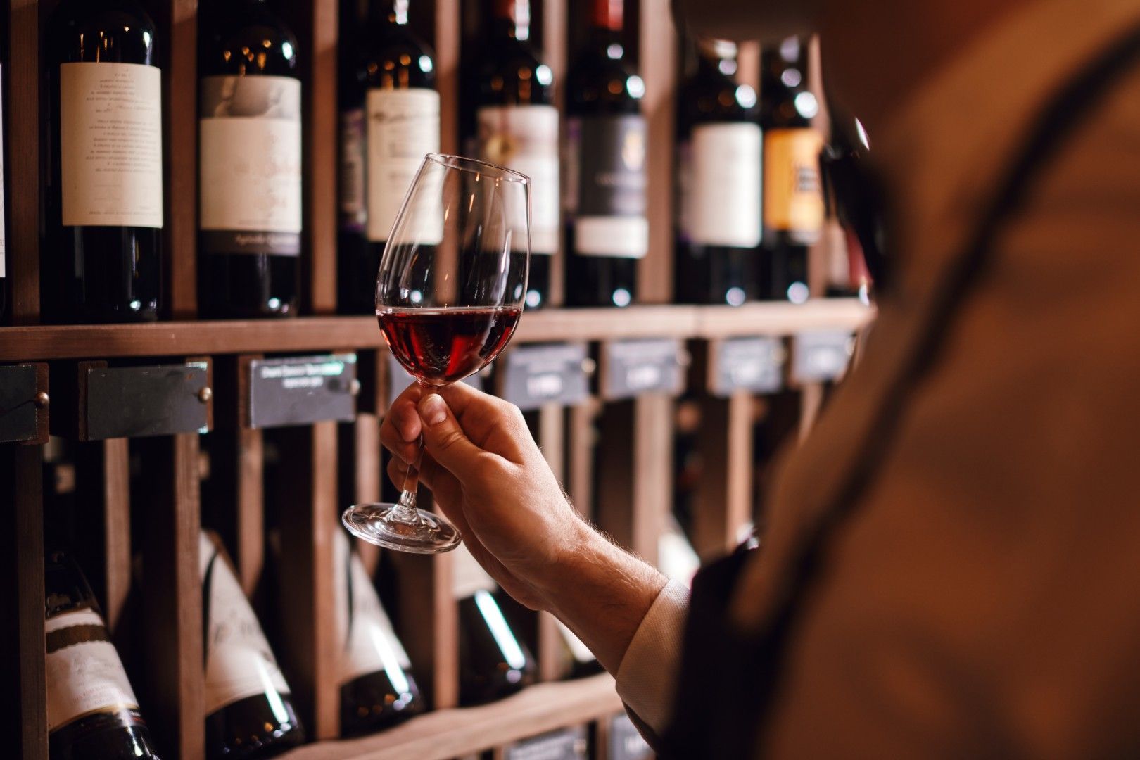 Main tenant un verre de vin devant un casier à bouteilles dans une cave sombre