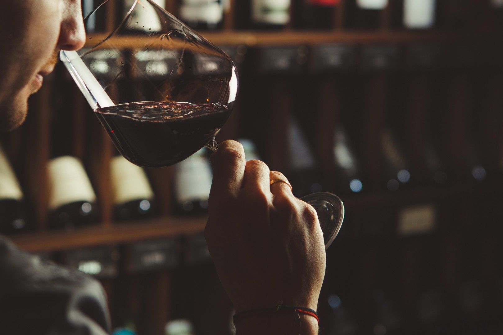 Une personne qui déguste du vin rouge dans une cave à vin tamisée, avec des bouteilles sur des étagères en arrière-plan