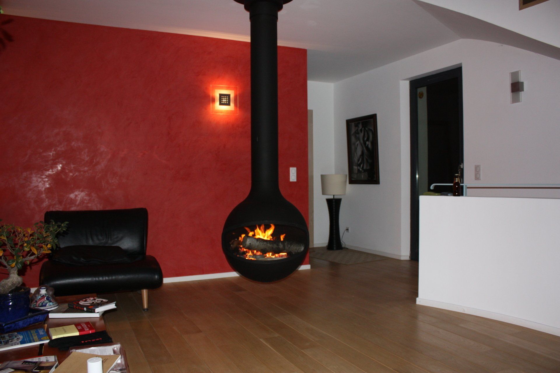 Cheminée sphérique noire suspendue au plafond du salon, avec un mur d'accent rouge.