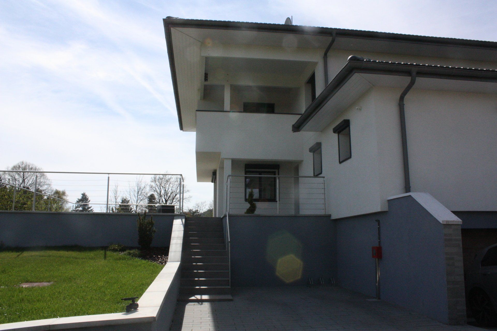 Maison blanche à deux étages avec balcon, escalier et petit jardin, par une journée ensoleillée.