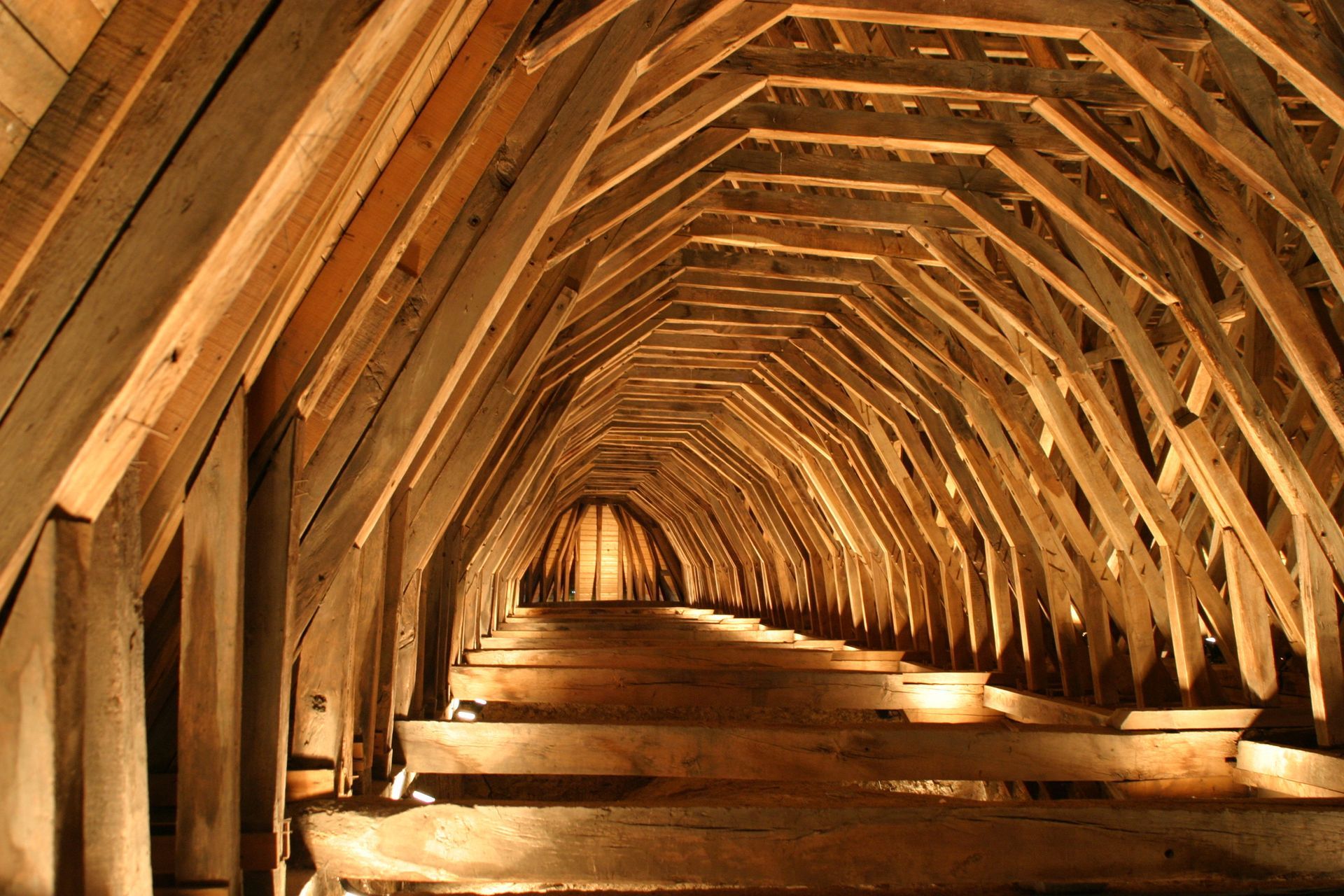 Structure mansardée en bois avec des arches répétitives s'étendant au loin, éclairée par en dessous.