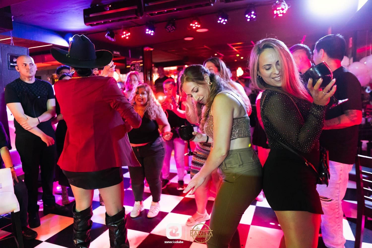 Gente bailando en un club iluminado con luces de neón rosas y moradas.