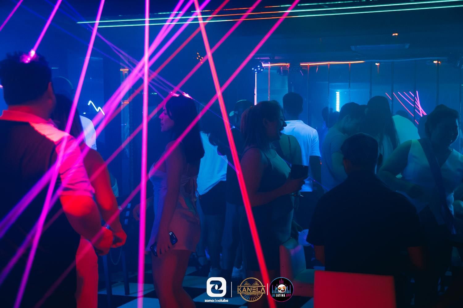 Gente bailando en una discoteca iluminada con luces de neón, rayos láser rosas y luces azules.