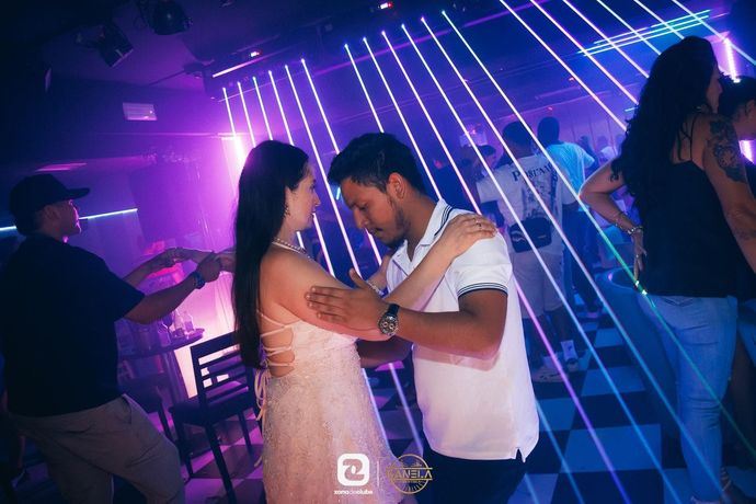 Una pareja baila muy junta en una discoteca iluminada con luces violetas y rayos láser de fondo.