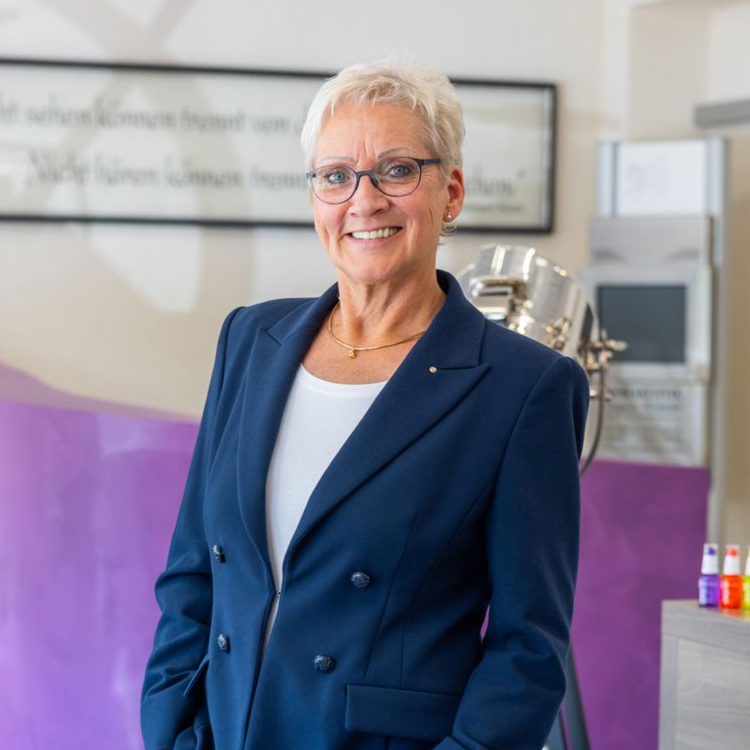 Eine Frau mit Brille und einer Halskette lächelt in die Kamera .