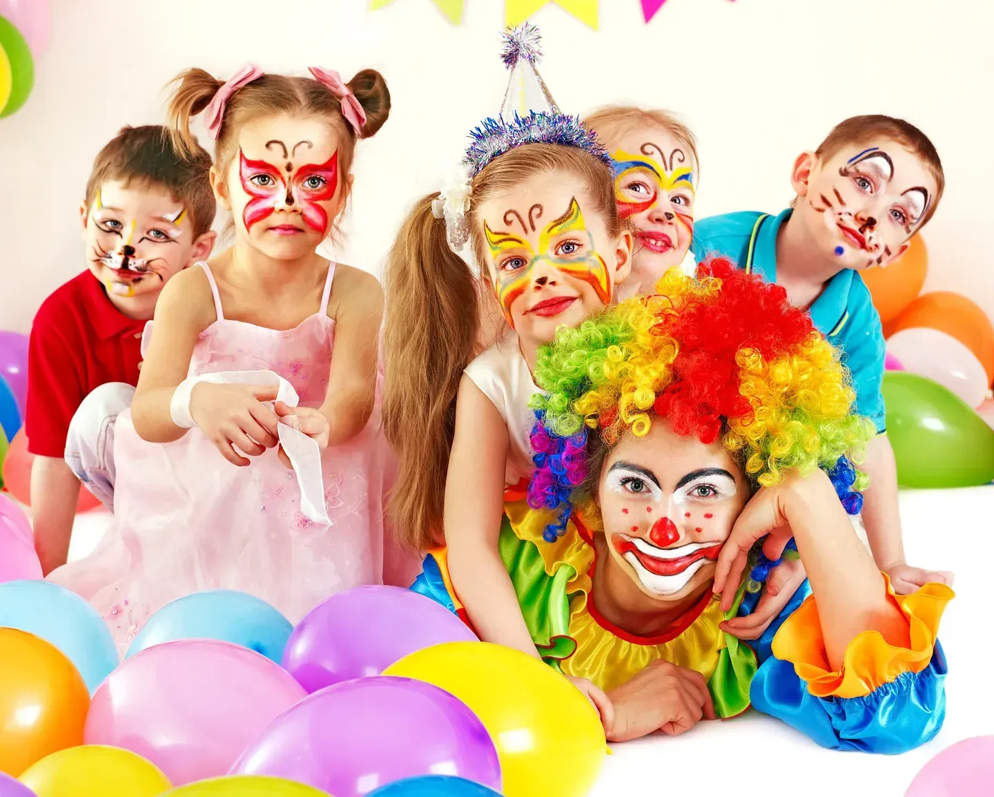 Un grupo de niños con las caras pintadas y un payaso con globos al fondo.