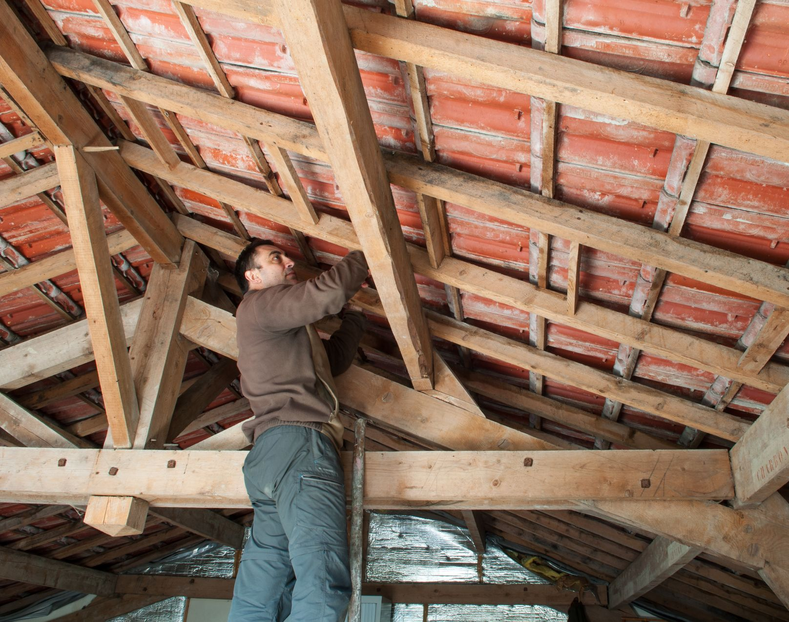 Homme travaillant sur une structure de toit en bois avec des tuiles en terre cuite.