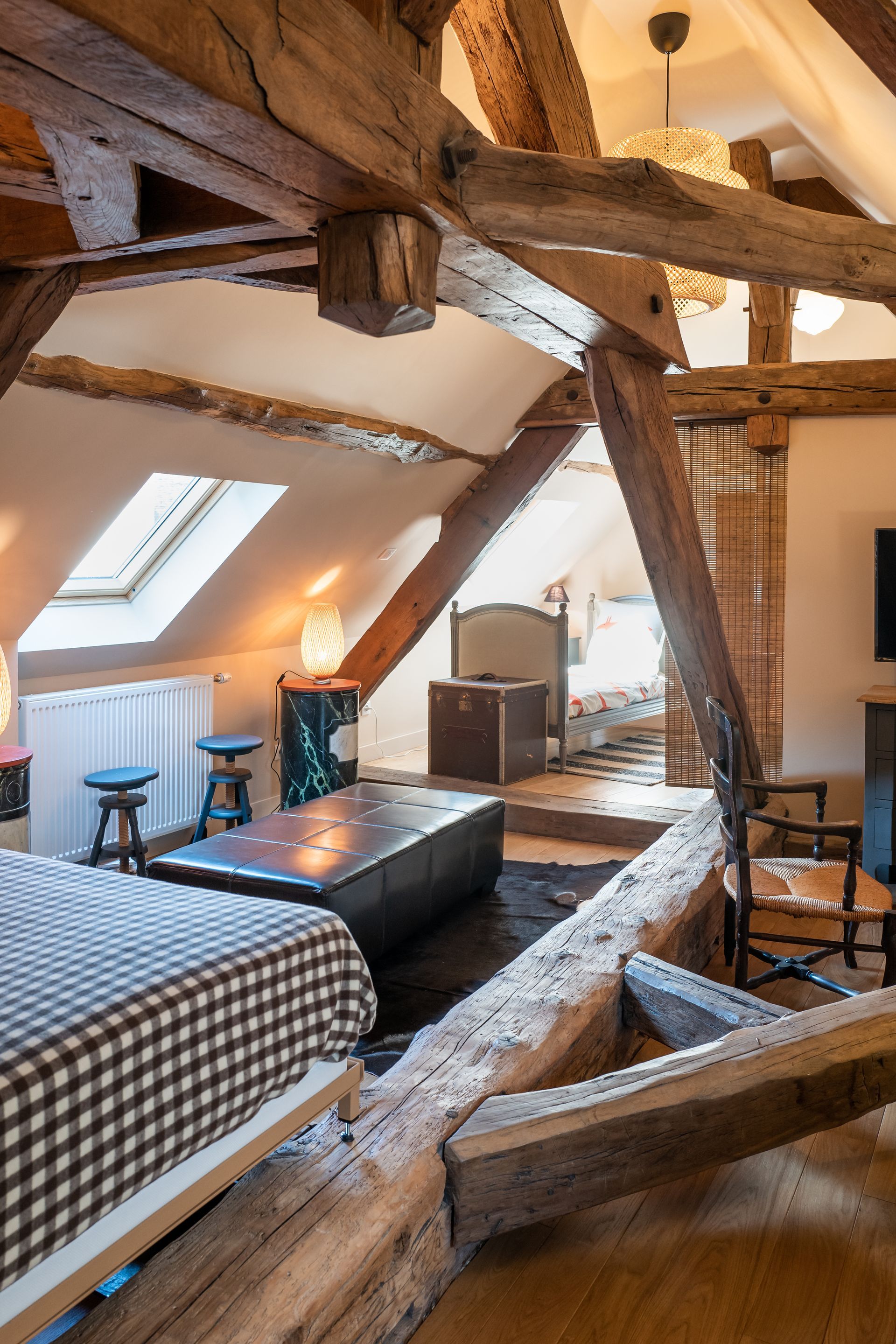 Chambre mansardée avec poutres apparentes, un lit et un puits de lumière.