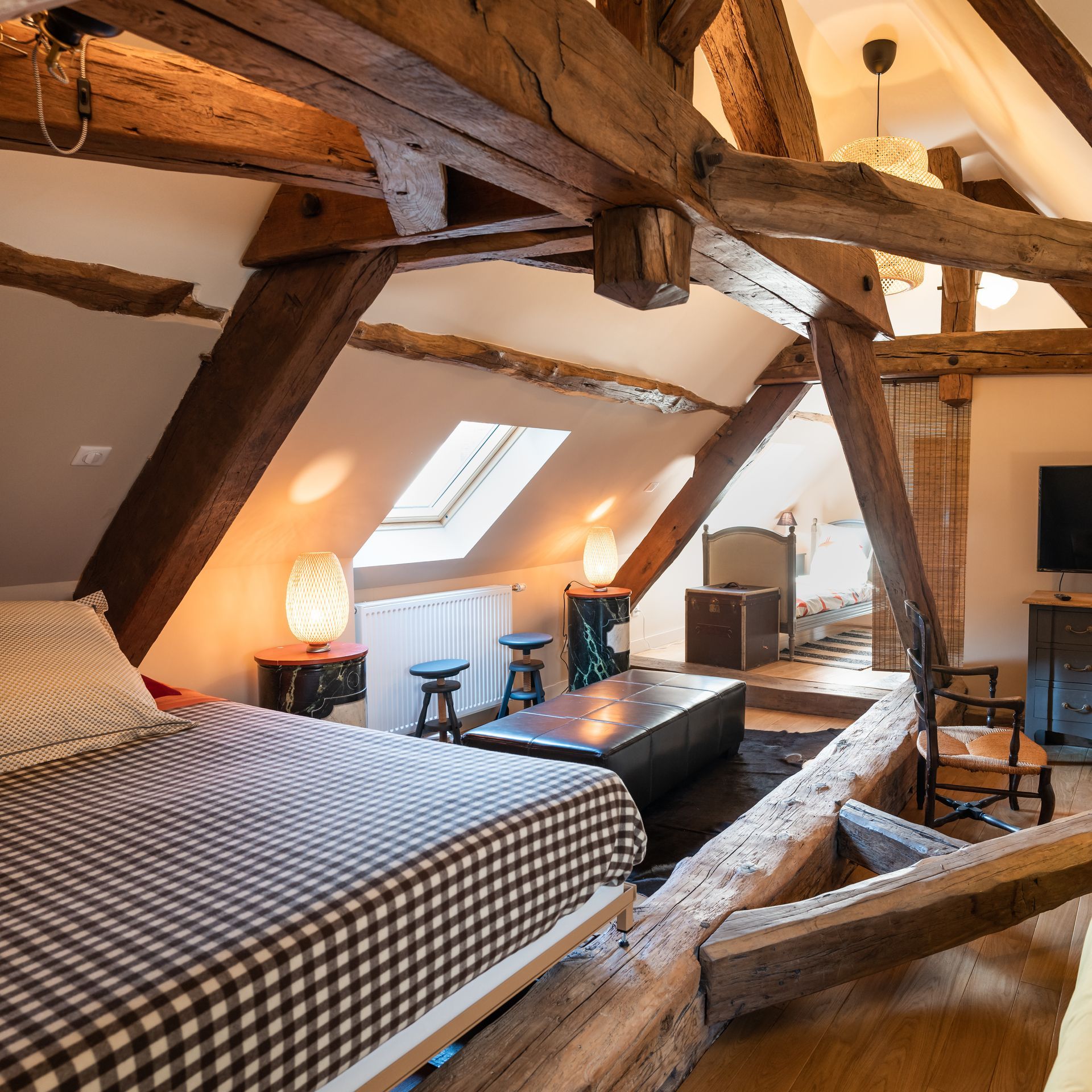Chambre mansardée avec poutres apparentes, lit et puits de lumière.