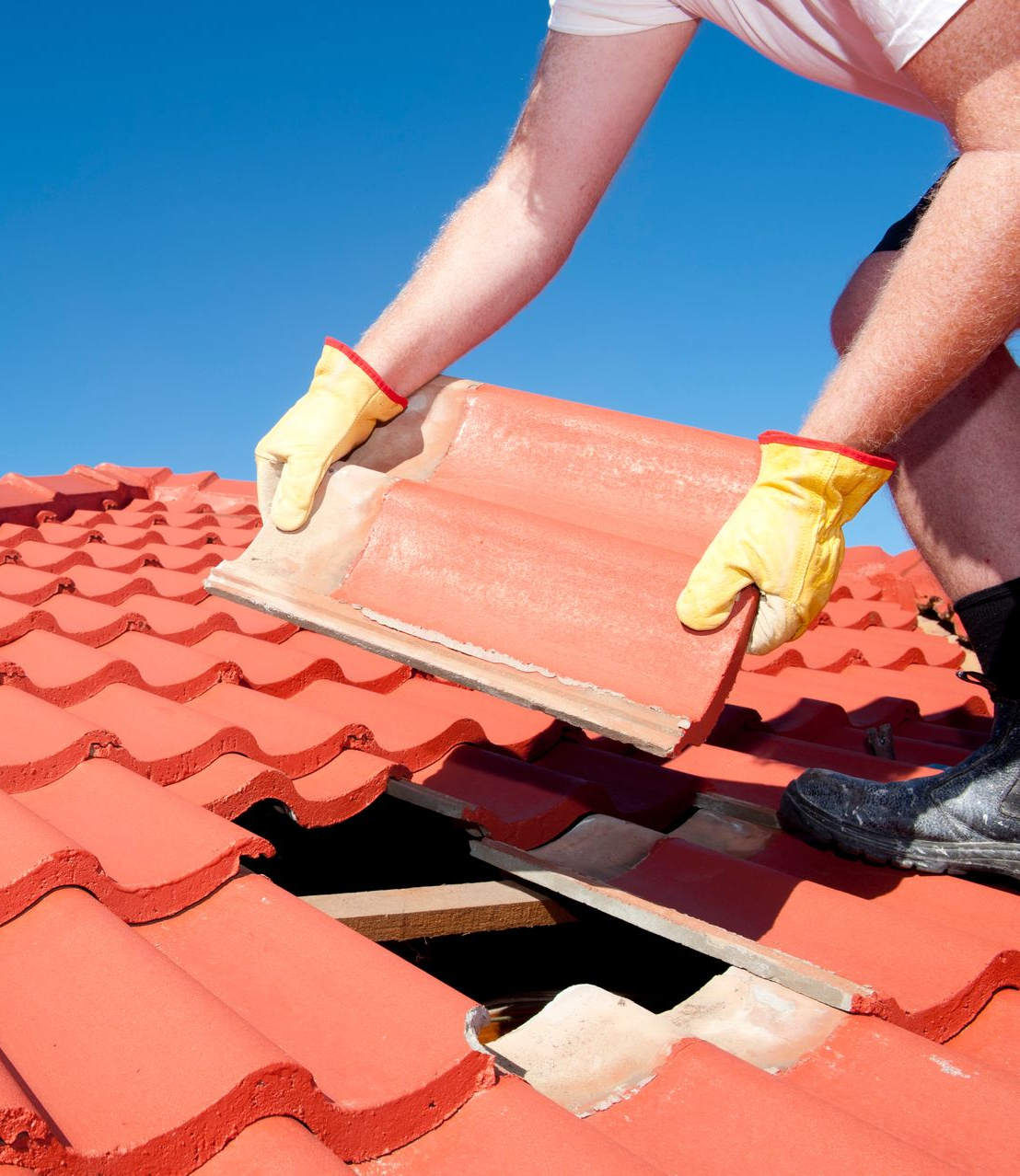 Une personne portant des gants jaunes remplace une tuile rouge par une journée ensoleillée.