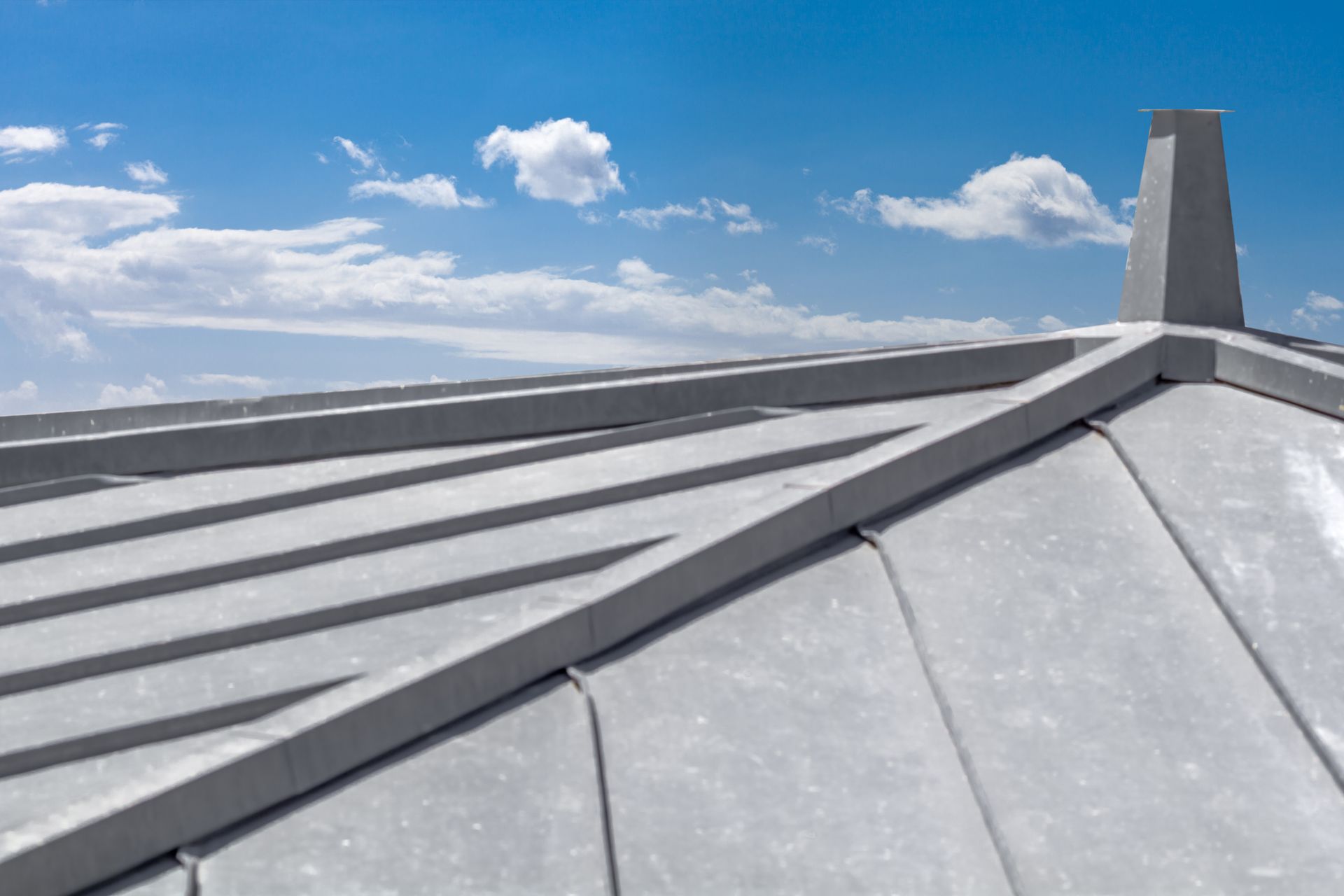 Gros plan d'un toit en métal gris avec une cheminée contre un ciel bleu avec des nuages.