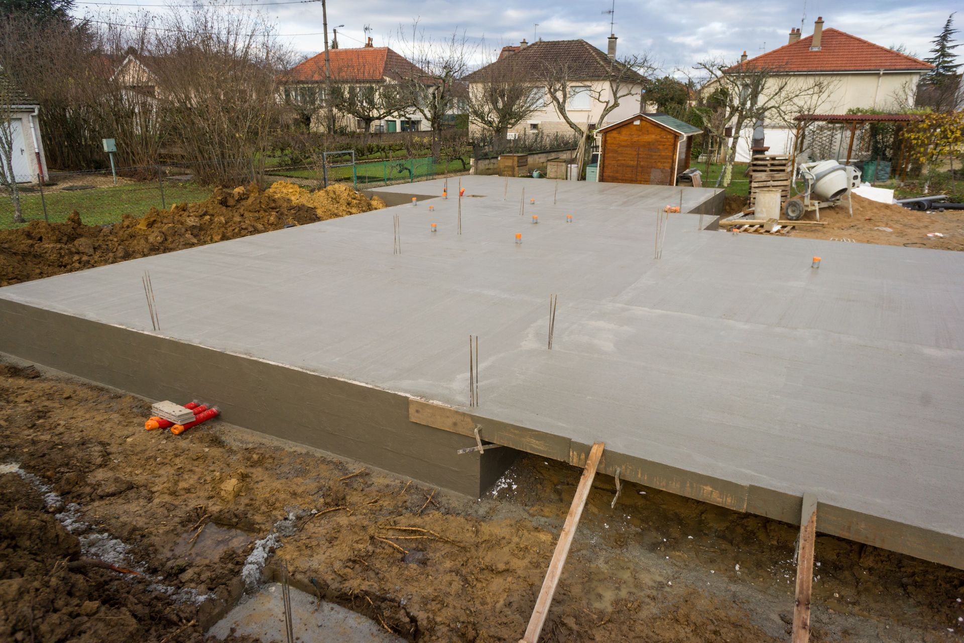 Fondations en béton fraîchement coulée ; chantier de construction avec des maisons en arrière-plan.
