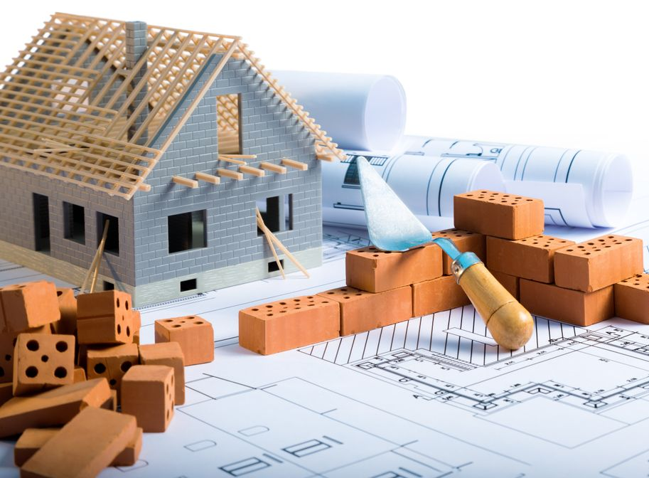 Modèle de maison en construction avec briques, plans et truelle.