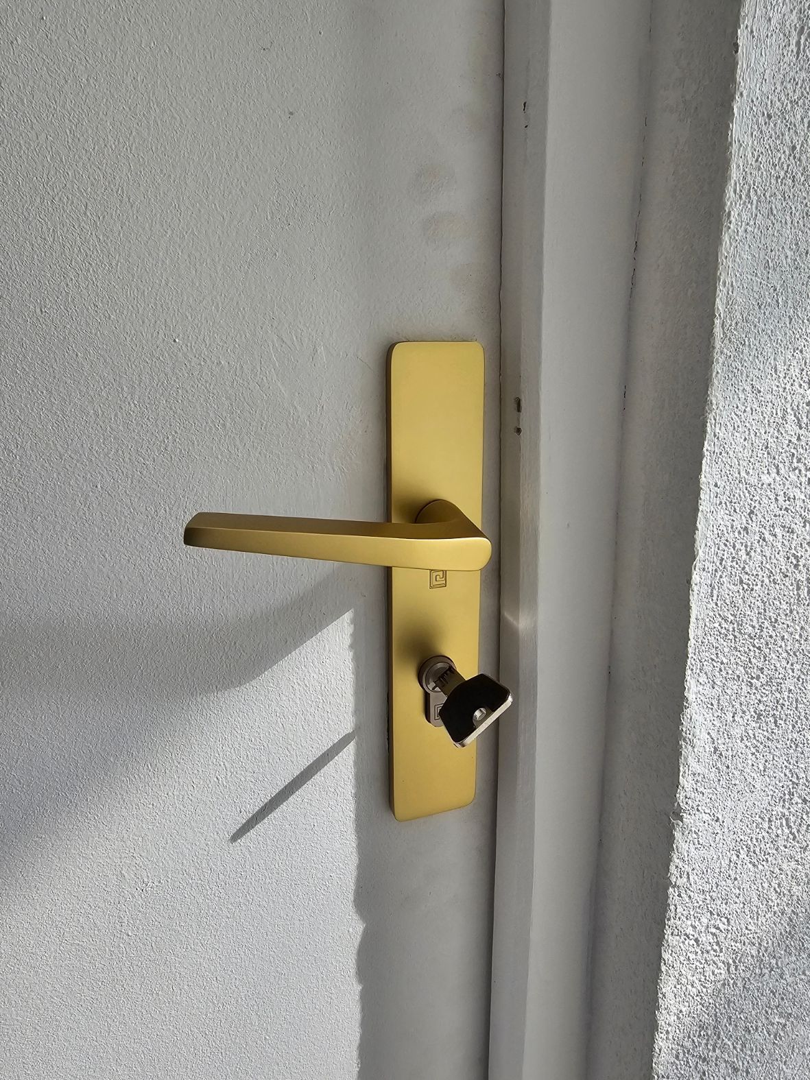 Poignée de porte et verrou en laiton sur une porte blanche, la porte étant partiellement ouverte et laissant apparaître le loquet.