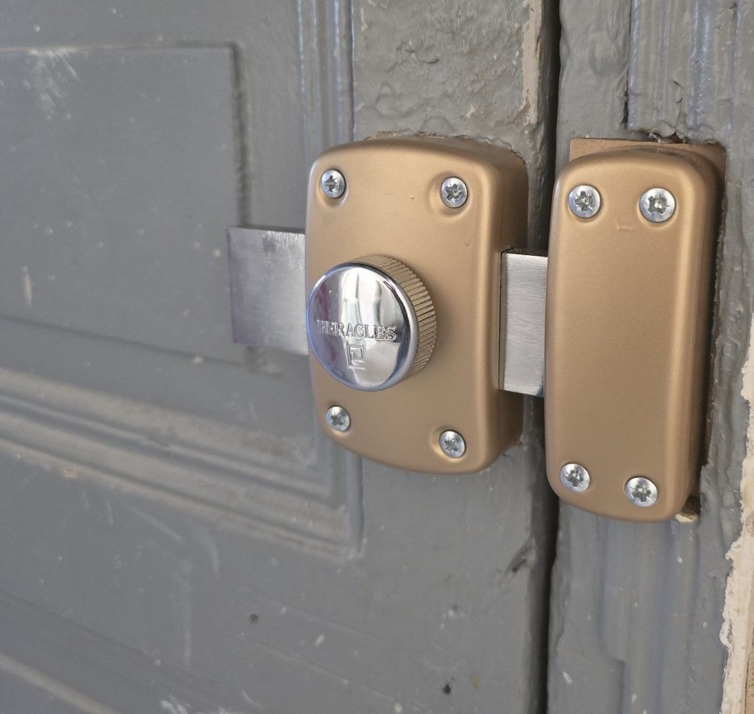 Poignée et serrure dorées sur une porte extérieure blanche.