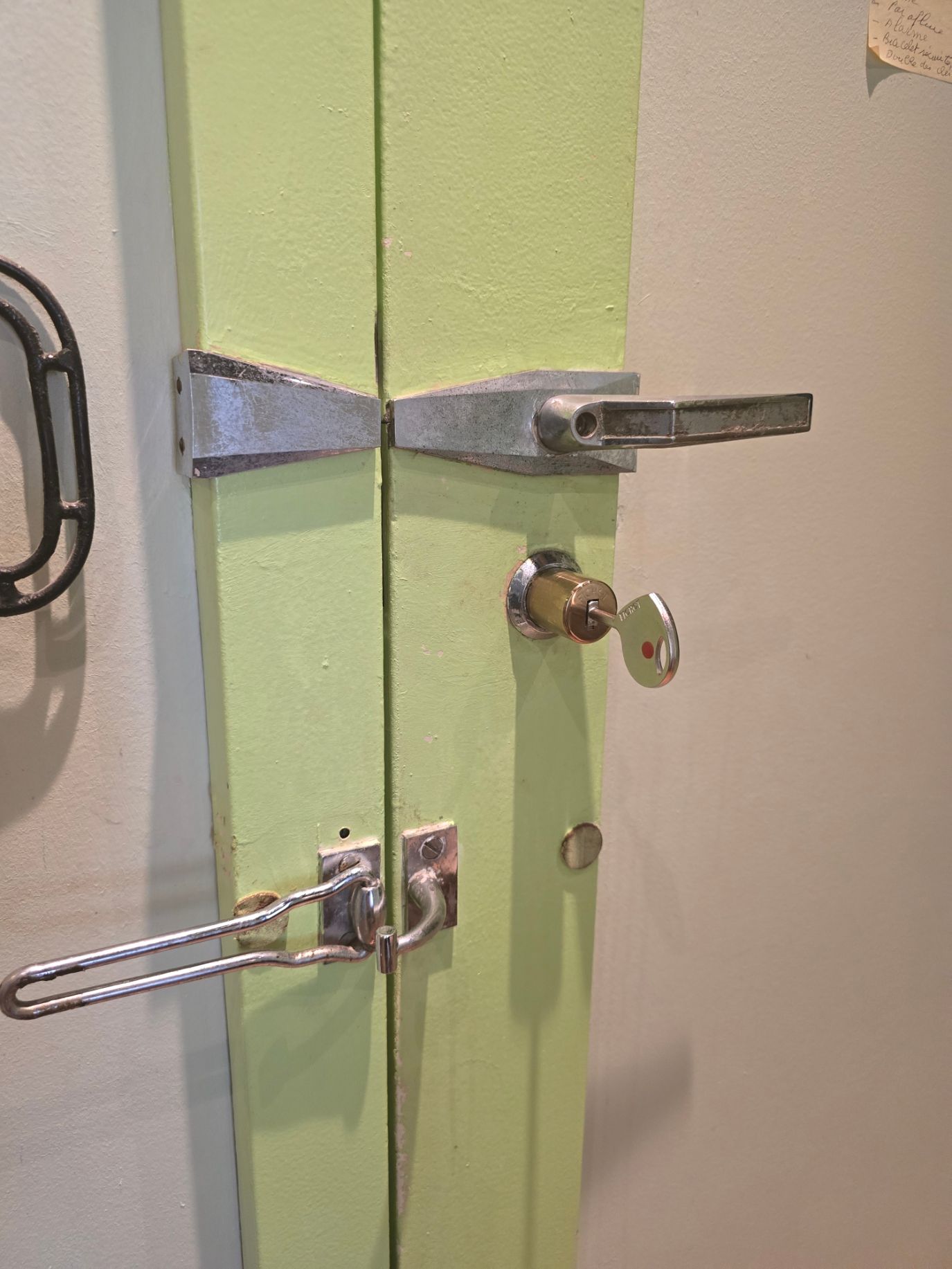 Poignée de porte blanche avec interrupteur de verrouillage rouge sur une porte vitrée près d'un panneau d'entrée à clavier