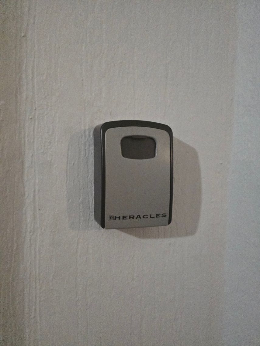 Gros plan sur un loquet de porte en laiton fermant une porte d'armoire blanche, avec un miroir reflétant un couloir.