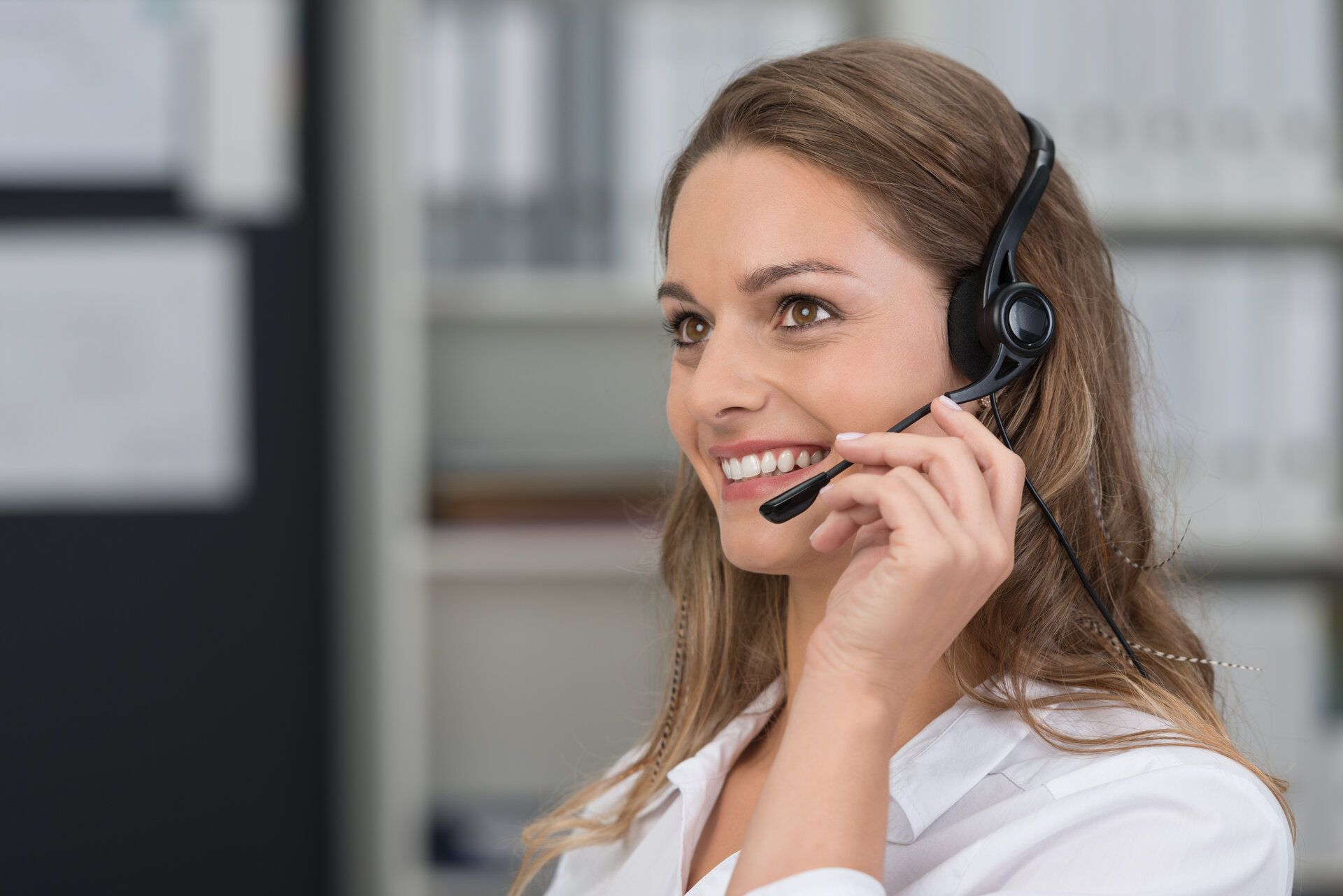 Eine Frau trägt ein Headset und lächelt, während sie telefoniert.