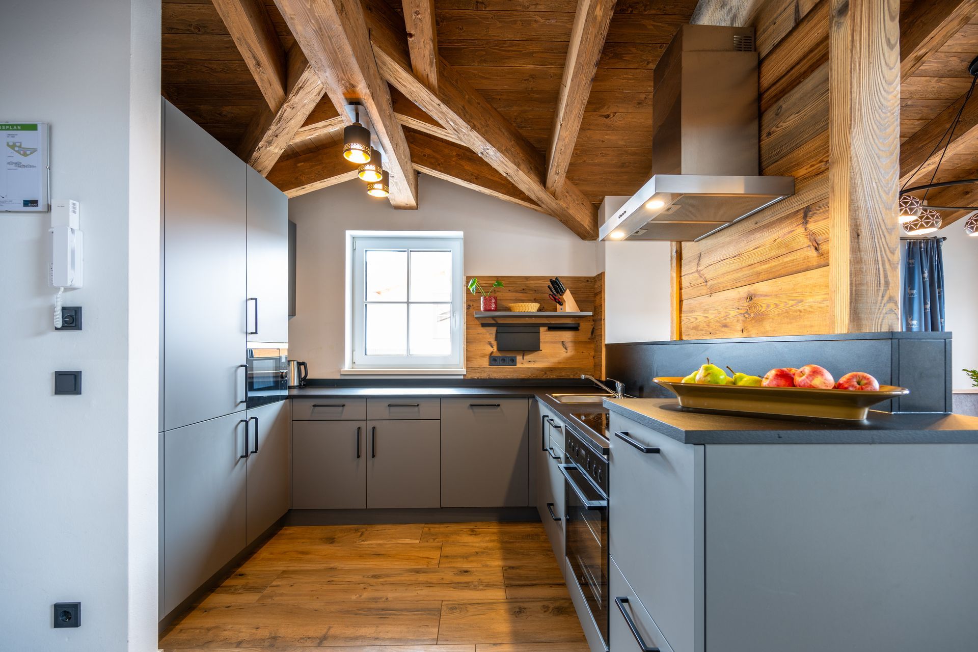 Graue Küche mit Holzbalken und -böden, einem kleinen Fenster und modernen Geräten.