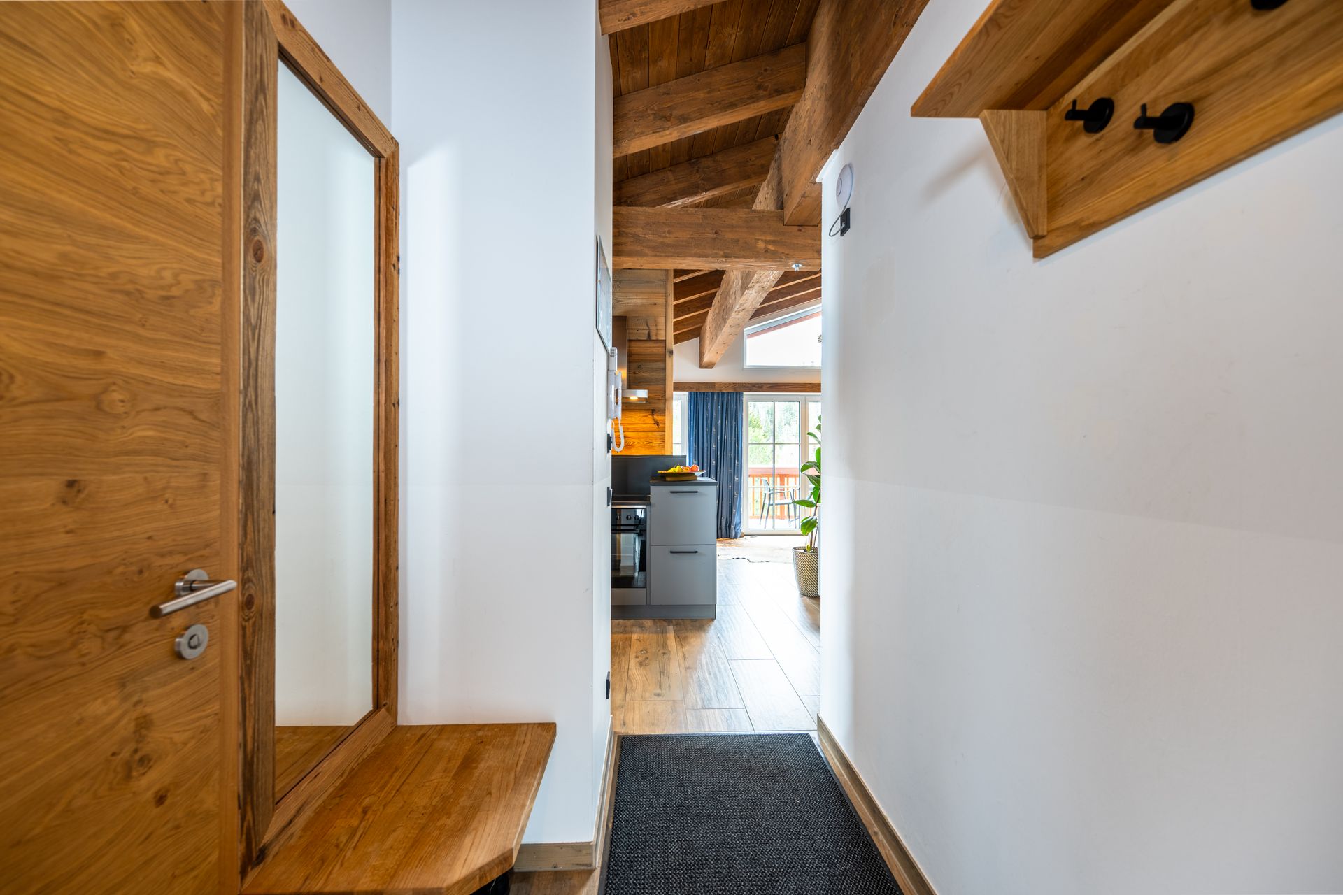 Flur mit Holztür und Spiegel, der zur Küche und zum Blick ins Freie führt.