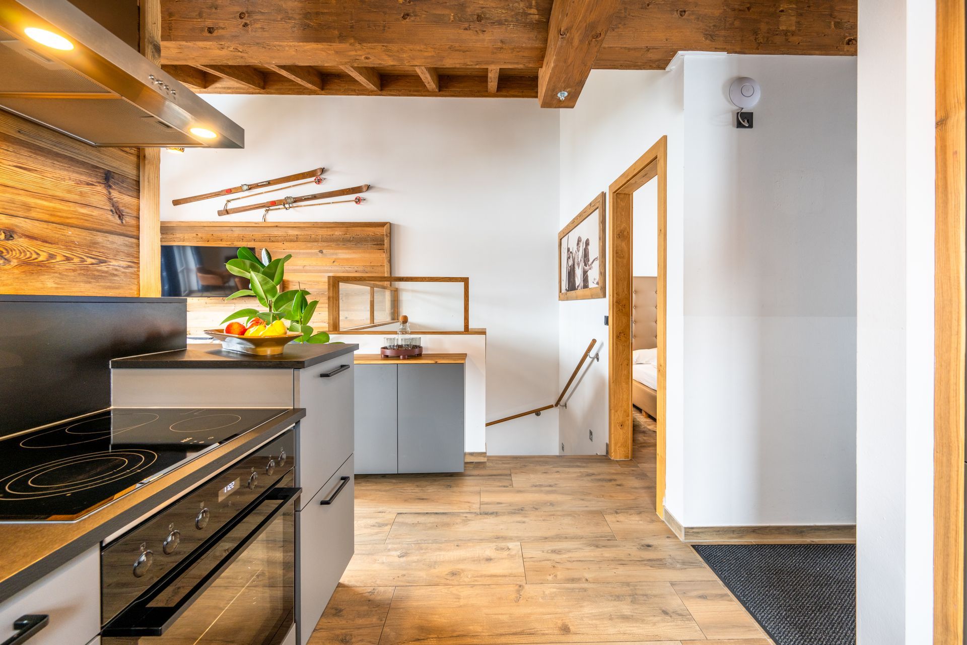 Innenraum einer Küche mit Holzbalken, hellen Holzböden und Schränken in neutralen Farben.