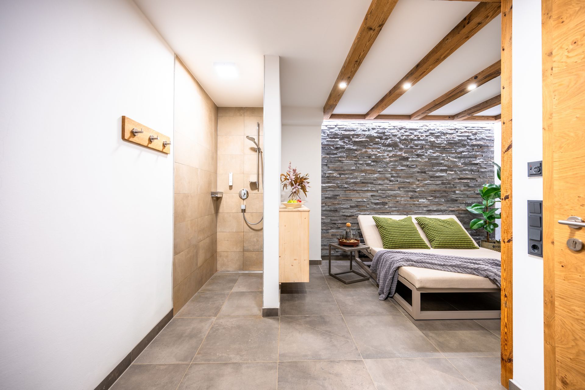 Ein Spa-Raum mit Dusche, Liegestuhl und Akzentwand aus Stein. Neutrale Töne mit Holz und Grün.