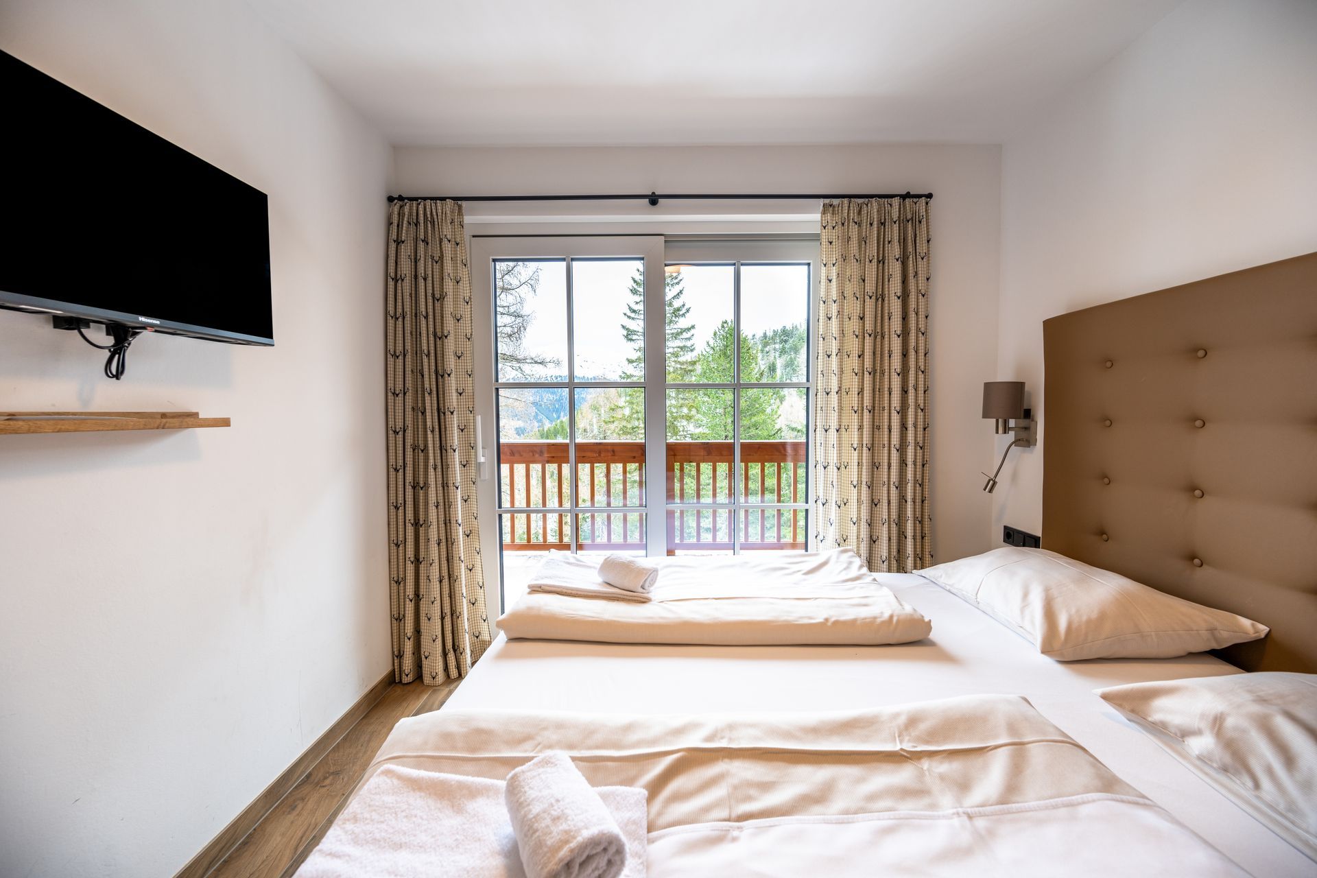 Schlafzimmer mit Bett, Balkonblick, an der Wand montierter Fernseher.