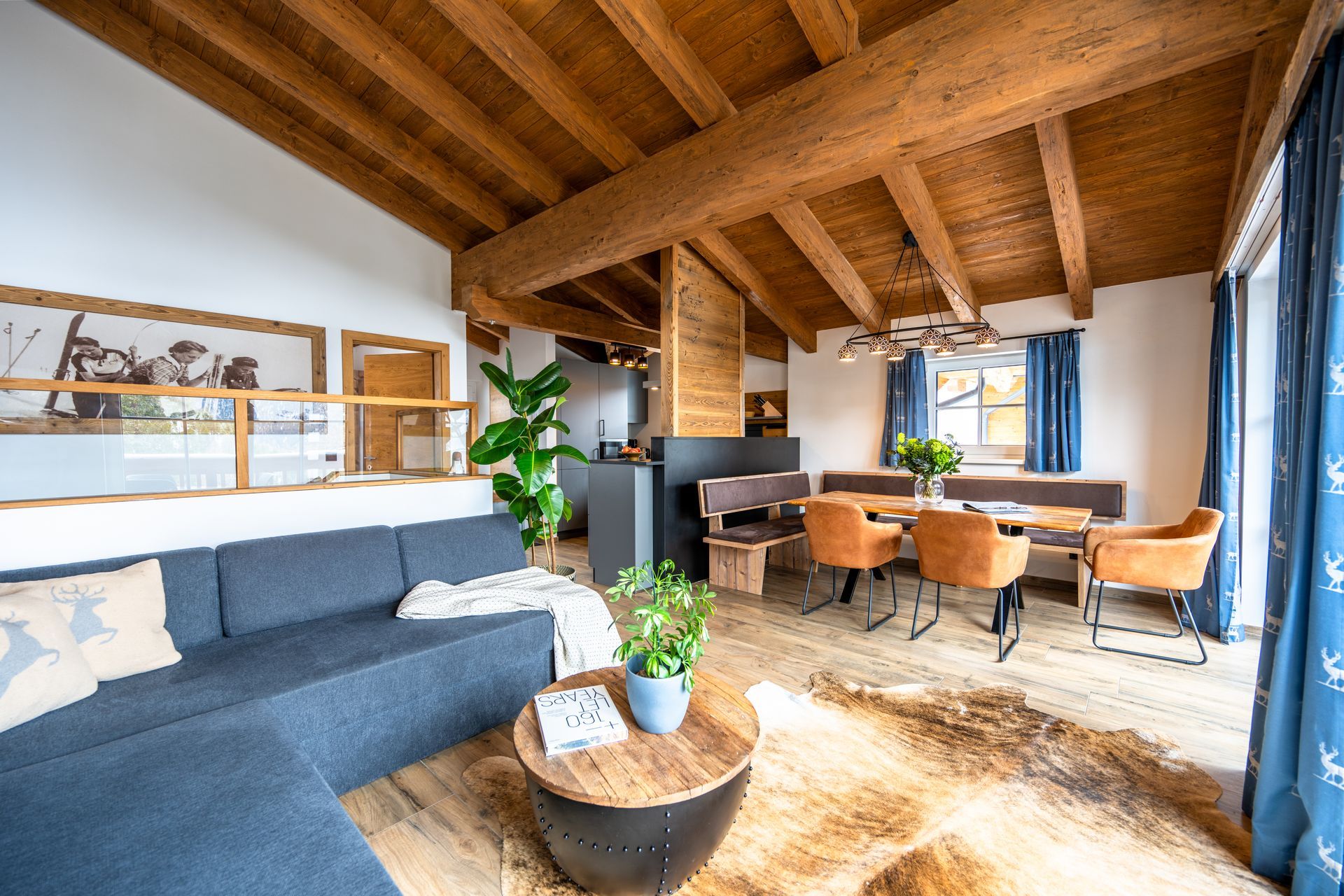 Wohnzimmer mit Holzbalken, blauem Sofa, Essbereich und einem Fellteppich.