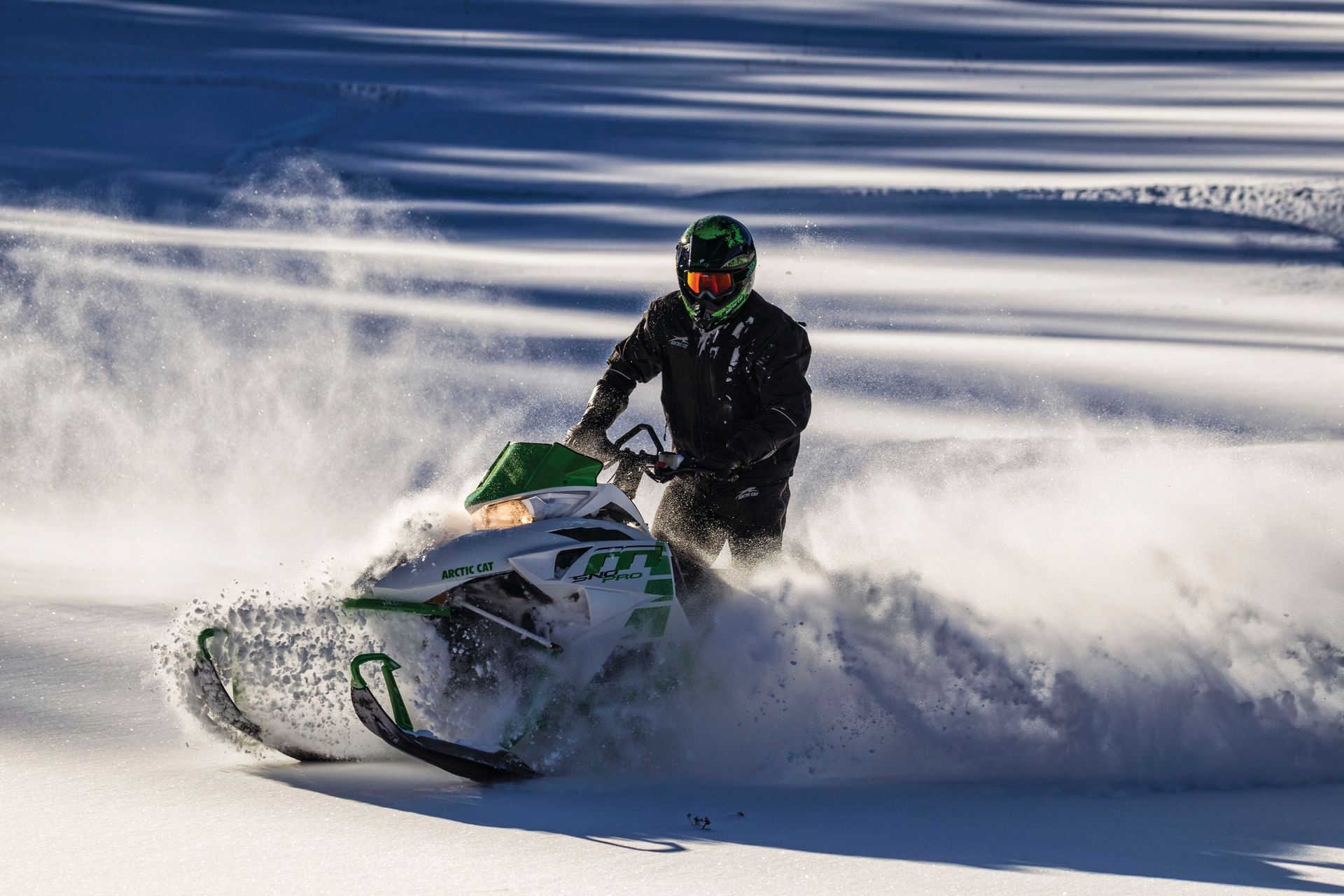 Schneemobilfahrer auf einem weißen Schneemobil wirbelt in einer sonnigen, verschneiten Umgebung Schnee auf.