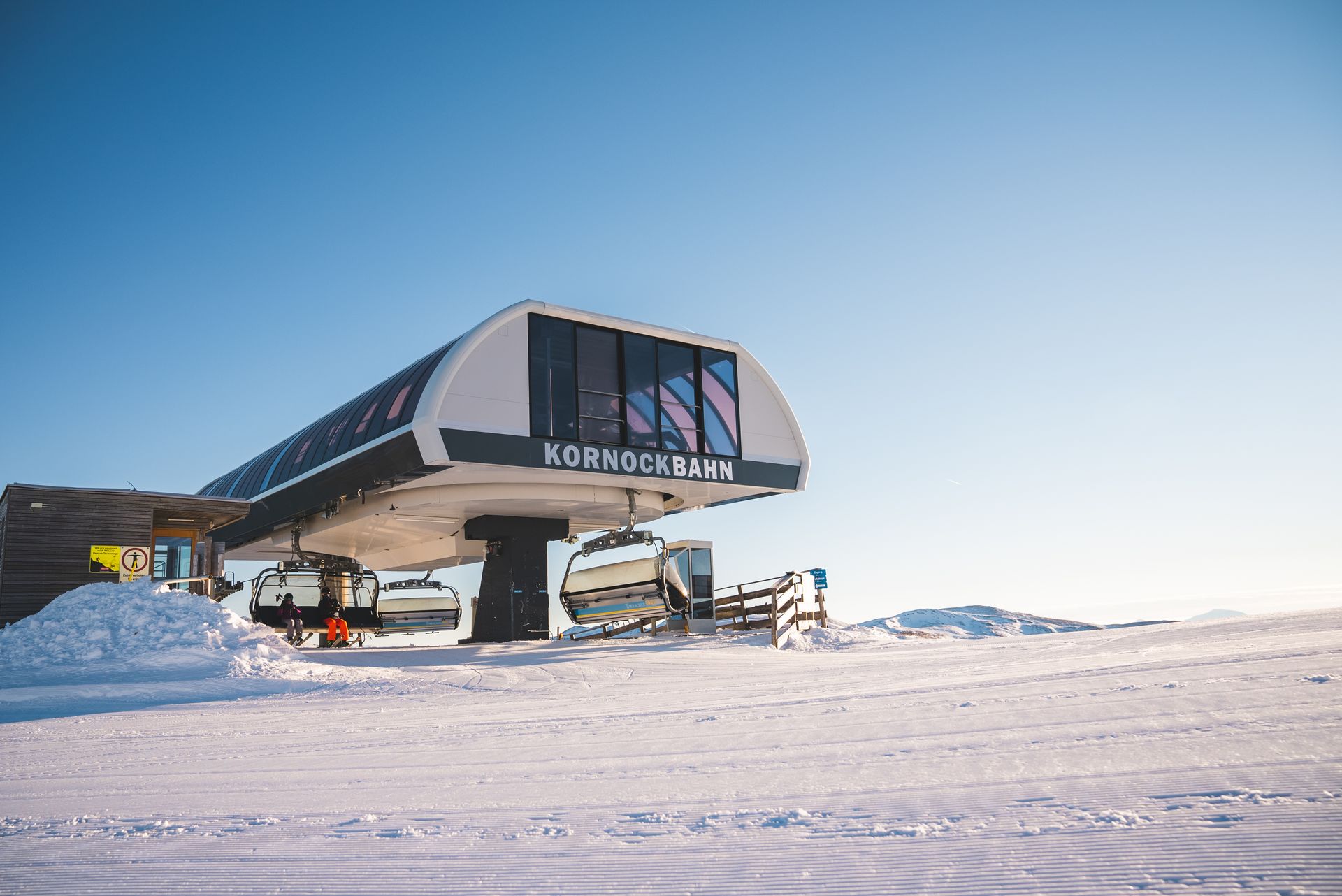 Skiliftstation an einem schneebedeckten Hang unter strahlend blauem Himmel. Auf dem Bauwerk ist „Ken McInnes“ zu sehen.