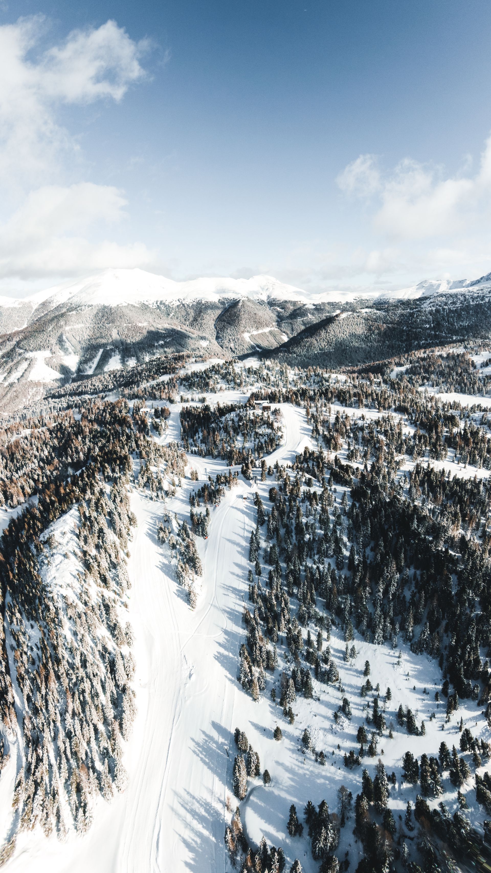 Verschneite Berglandschaft mit Skipisten und Wald unter blauem Himmel.