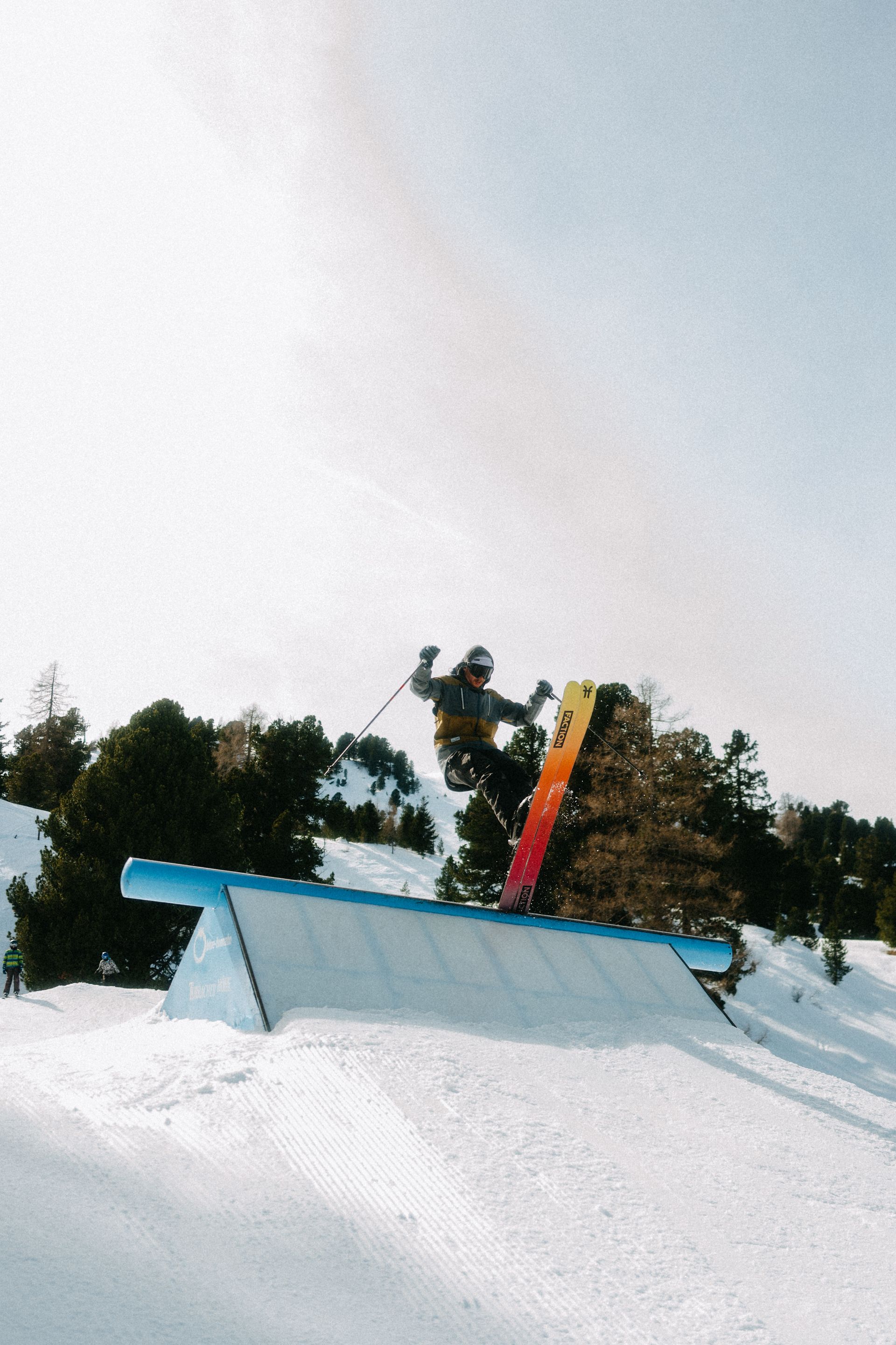 Skifahrer in der Luft über einer Schienenkonstruktion in einem verschneiten Terrainpark unter einem strahlenden Himmel.