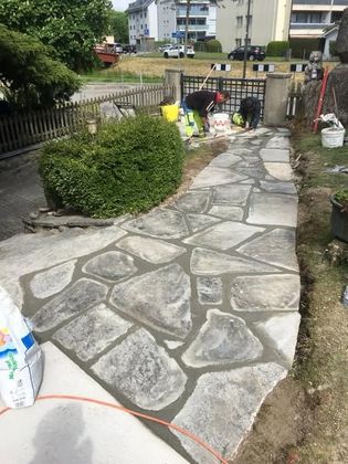 An einem sonnigen Tag schlängelt sich ein Steinweg durch grünen Rasen zu einem mehrstöckigen Wohnhaus.