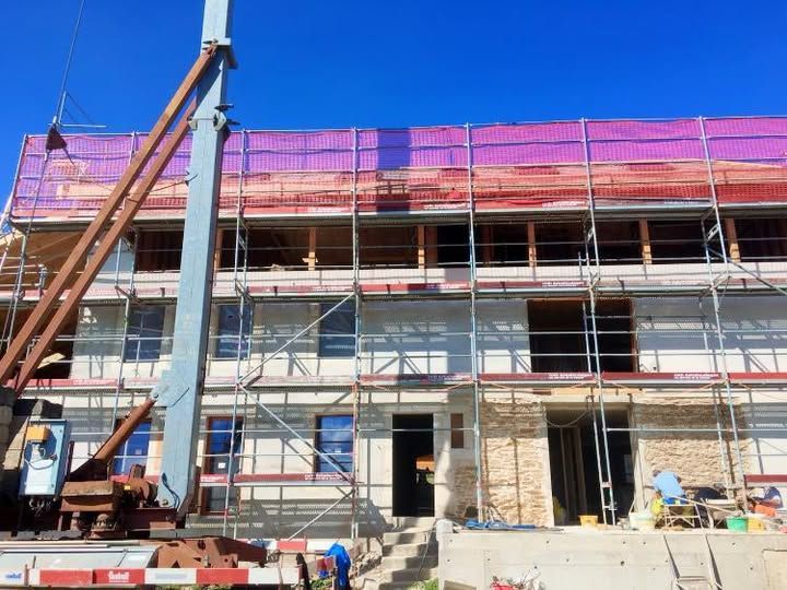 Innenansicht eines Büroraums, der gerade renoviert wird, mit freiliegenden Deckengittern, Baumaterialien und unfertigen Wänden.