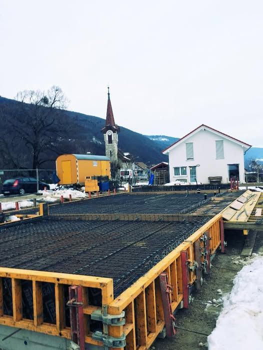 Ein im Bau befindliches zweistöckiges Haus mit Gerüst, umgeben von einer grünen Wiese und einem bewölkten Himmel.