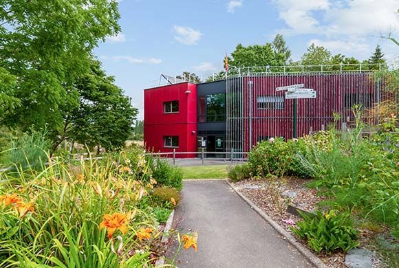 Bâtiment moderne rouge et noir avec un chemin de jardin et des fleurs colorées.