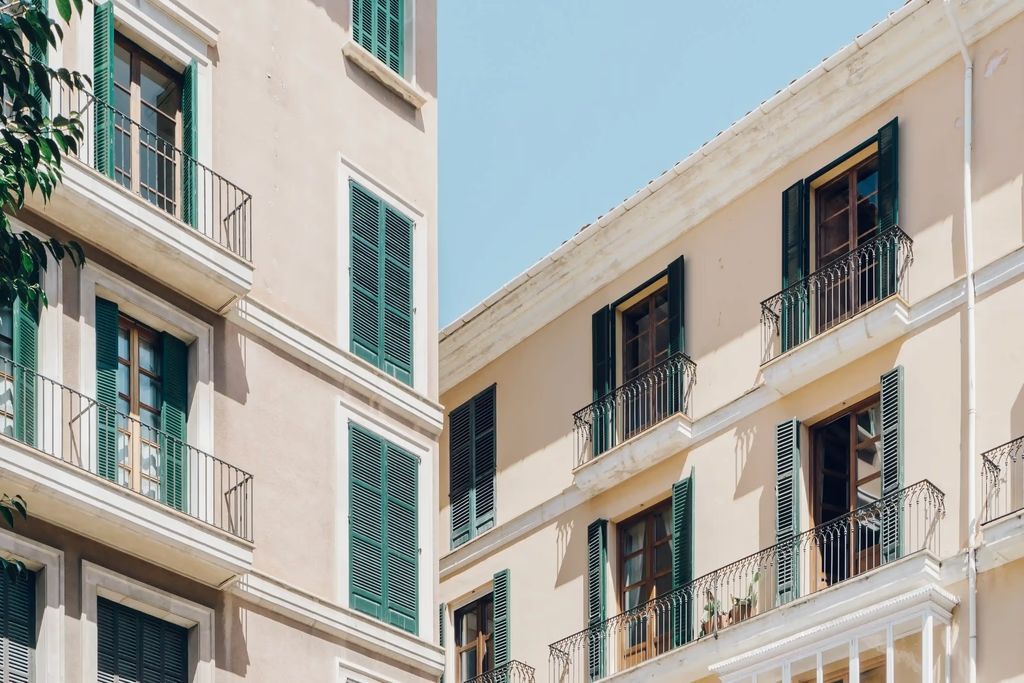 Edificios de apartamentos en tonos pastel con contraventanas y balcones verdes contra un cielo azul claro.