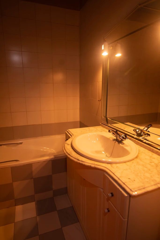 Baño con lavabo, espejo, bañera e iluminación cálida.