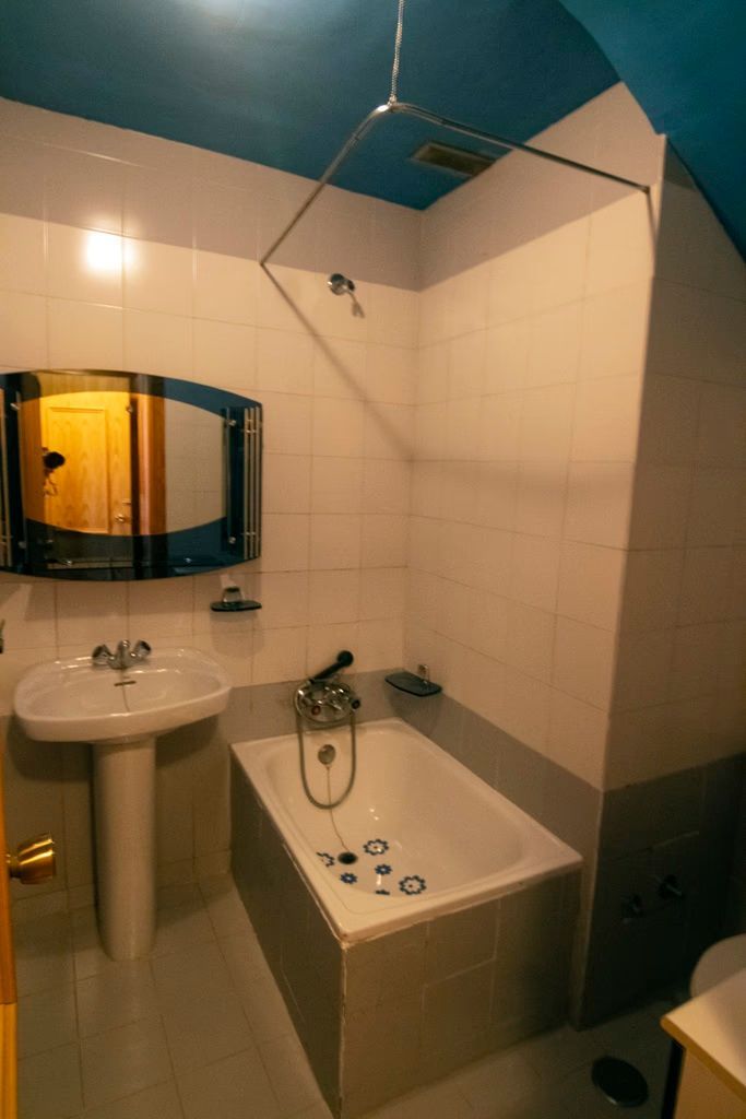 Baño pequeño con lavabo, espejo y bañera bajo un techo azul.