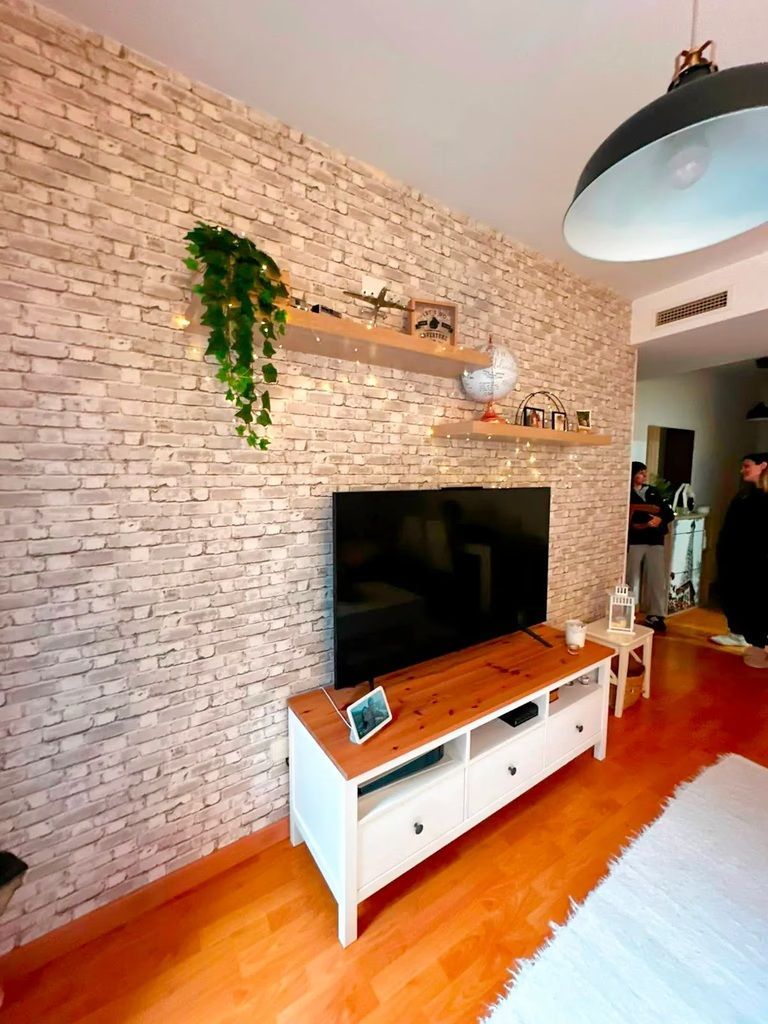 Sala de estar moderna con pared decorativa de piedra, televisor montado en la pared, consola de madera y planta colgante.