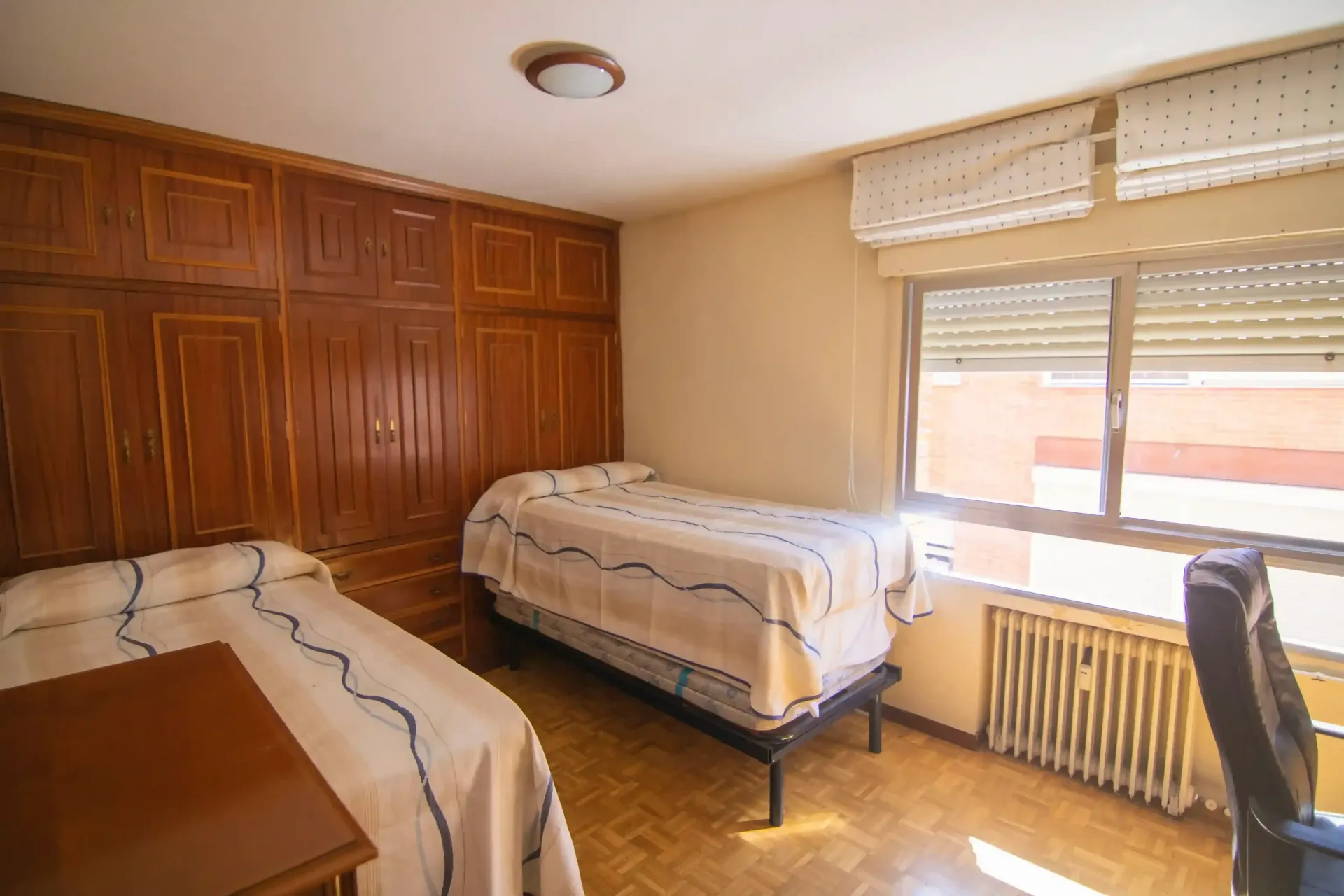Habitación pequeña con dos camas individuales, armarios empotrados de madera y una ventana con persianas.