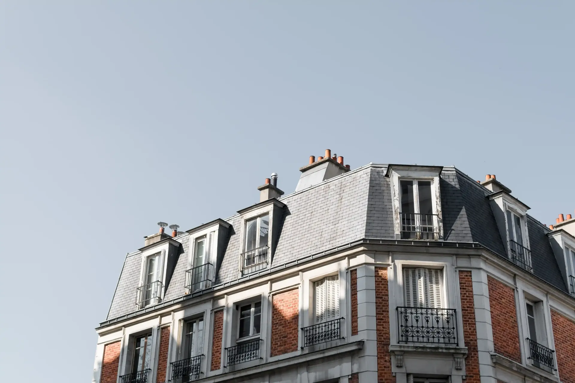 Parte superior de un edificio parisino de ladrillo rojo con tejado abuhardillado gris contra un cielo despejado.