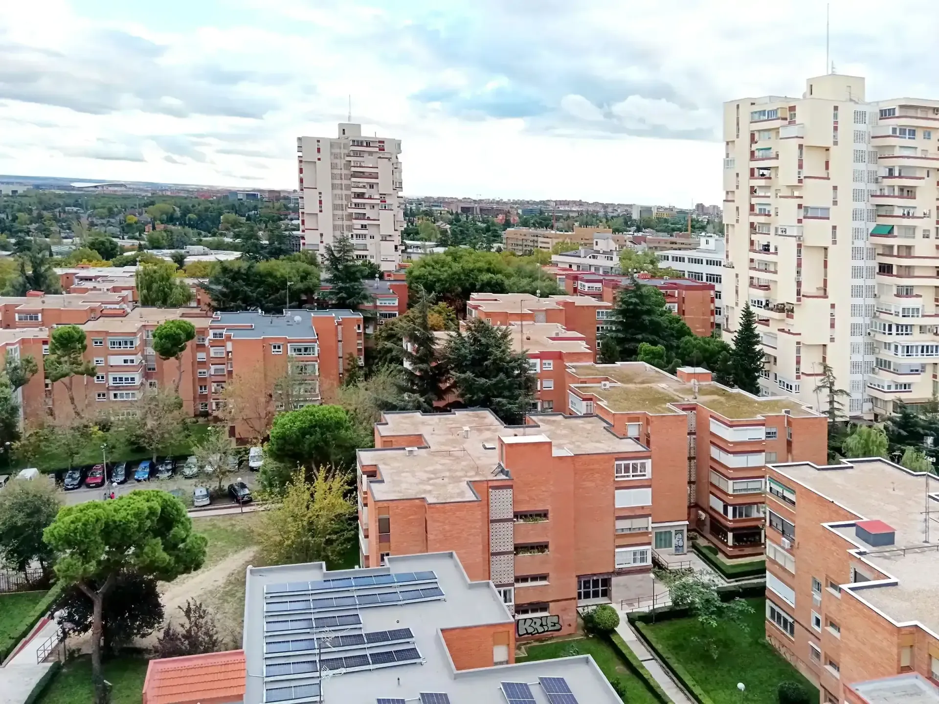 Vista desde un rascacielos sobre edificios de apartamentos de ladrillo rojo y árboles bajo un cielo nublado.