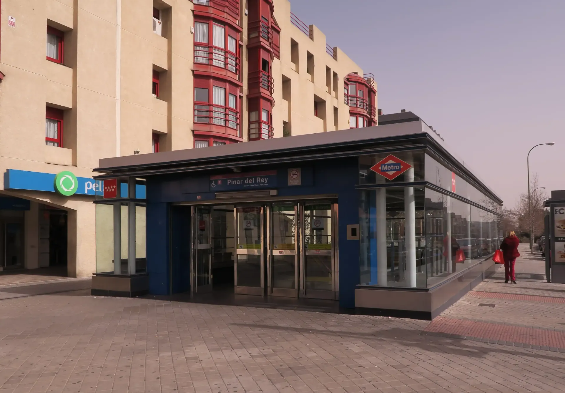 Un local comercial con fachada de cristal en una acera de la ciudad, junto a edificios de apartamentos rojos y beige.