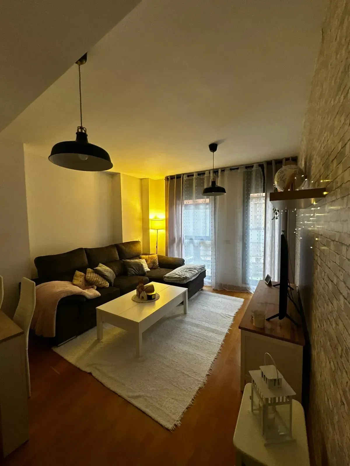 Acogedora sala de estar con sofá modular, mesa de centro, alfombra e iluminación cálida de color amarillo junto a la ventana.