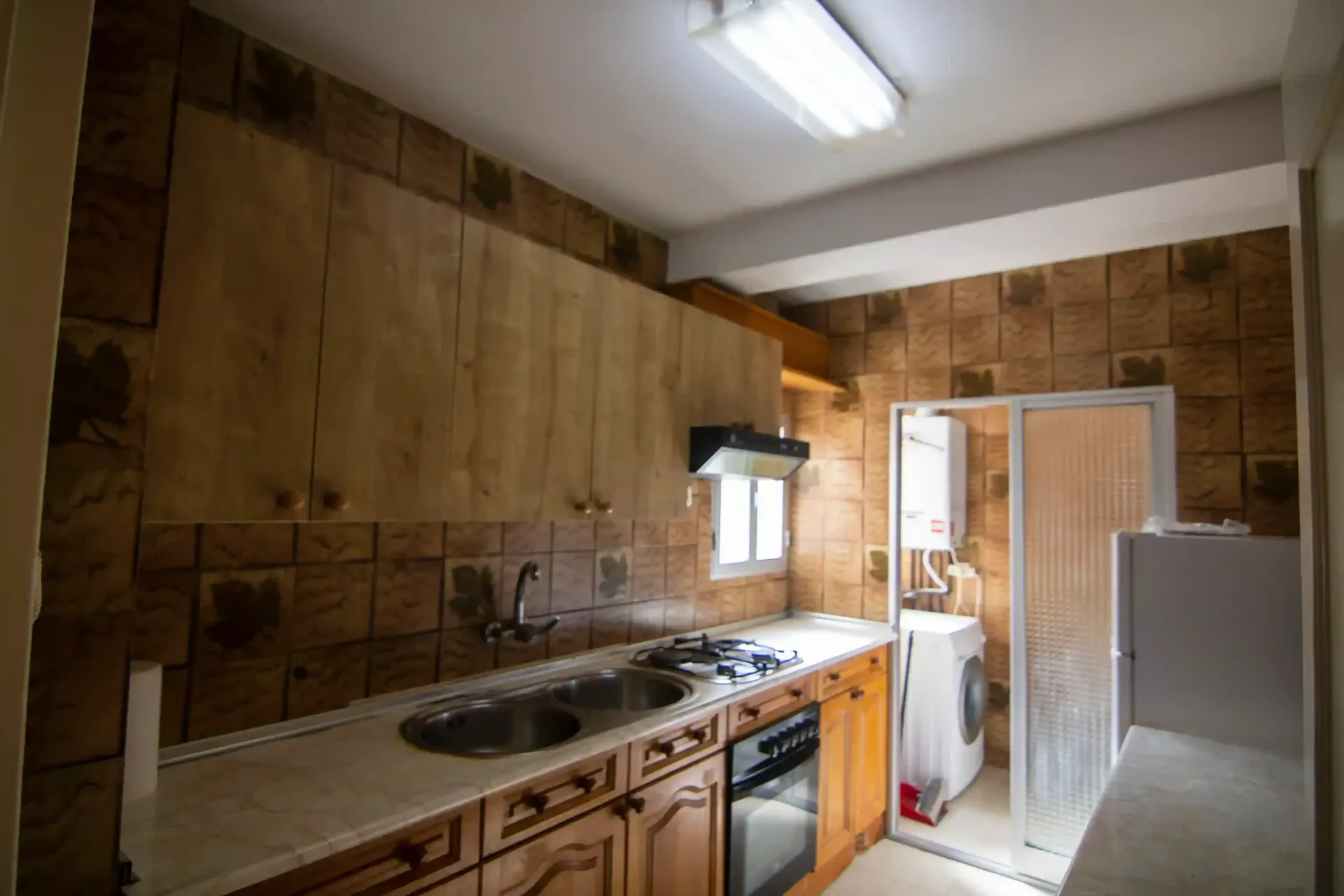 Cocina pequeña con paredes revestidas de madera, fregadero, estufa y puerta abierta a un área de lavandería.